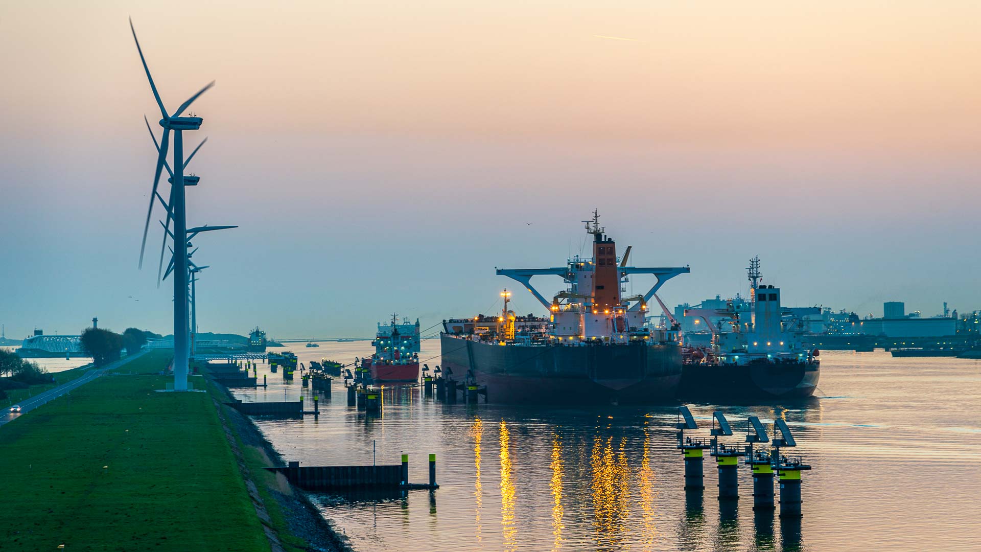 Multiple cargo vessels illuminated at dusk as they navigate a calm, industrial waterway—capturing the rhythm, scale, and coordination of modern port traffic and marine logistics.